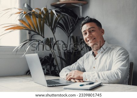 Good-looking millennial office employee in glasses sitting at desk in front of laptop smiling looking at camera. Successful worker, career advance and opportunity, owner of prosperous business concept Royalty-Free Stock Photo #2339801745