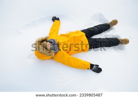 Top view of child doing snow angel. Little boy playing in snowdrift and having fun with fresh snow. Active outdoors leisure for kids on nature in snowy winter day.