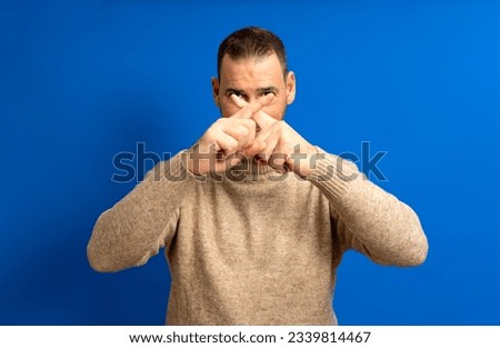 Hispanic man in his 40s crossing his fingers in stop and protest against the total oppression of the elites towards the proletariat, isolated on blue background. Royalty-Free Stock Photo #2339814467