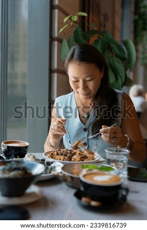 A young Asian woman sits eating pasta at a table in a cafe. High quality photo