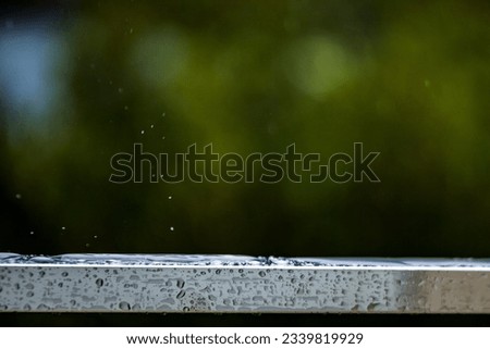 Raindrops falling on the surface of the parapet and bouncing in different directions on a blurred background of nature.