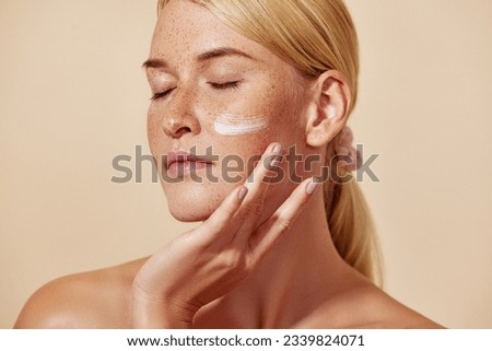 Beautiful young female with closed eyes applying white cream on her face  Royalty-Free Stock Photo #2339824071