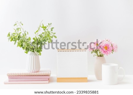 Mockup white desk calendar and pink flowers in a vase on a light background. Spiral calendar for mockup template advertising and branding
