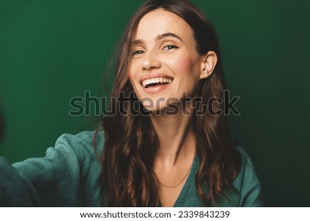 Portrait of young happy brunette curly hair woman with toothy smile laughing isolated over green wall background make selfie looking camera. Royalty-Free Stock Photo #2339843239