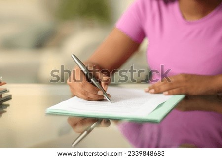 Close up portrait of a black woman hand filling form on a desk at home Royalty-Free Stock Photo #2339848683