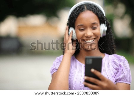 Front view portrait of a happy black woman listening to music in the street
