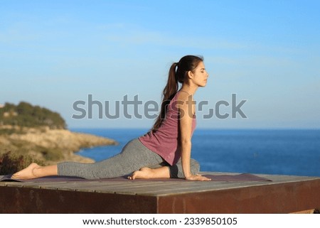 Side view portrait of a woman doing yoga in a wooden terrace on the beach Royalty-Free Stock Photo #2339850105