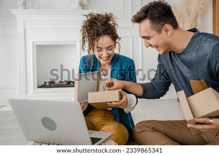 young couple man and woman boyfriend and girlfriend or husband and wife exchange gifts at home giving presents to each other and opening box happy smile celebrate valentine holiday or birthday Royalty-Free Stock Photo #2339865341