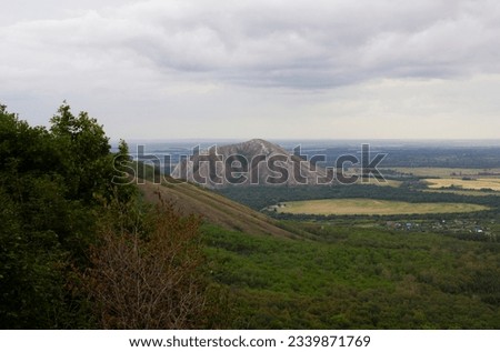 The green peak of a low mountain, overgrown with forest, next to which you can see another mountain, Shihan. Mixed tree species. Summer, Bashkiria, Russia Royalty-Free Stock Photo #2339871769