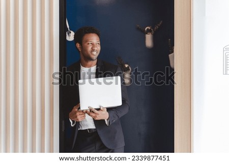 Confident african american business man wearing stylish formal suit holding laptop computer and looking away while standing at blue skype room in modern office  Royalty-Free Stock Photo #2339877451