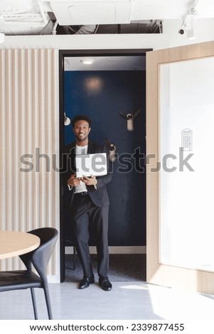 Confident African american business man wearing stylish formal suit holding laptop computer and looking at camera while standing at blue skype room in modern office  Royalty-Free Stock Photo #2339877455