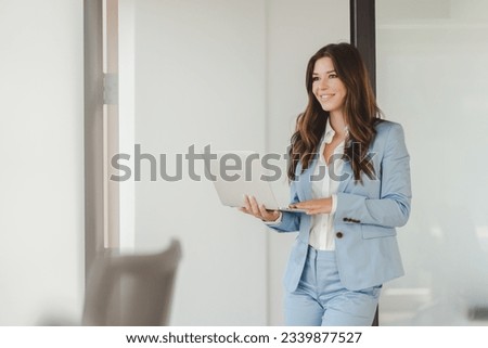 Positive confident smiling businesswoman professional manager using laptop, working online looking at screen in modern office. Freelancer copywriter typing standing at workplace. Technology concept 