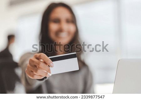 Cropped view of the blurred indian businesswoman holding credit card and showing it to camera while working in modern office. Online banking concept
