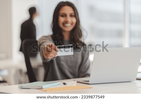Glad indian woman looking at camera and showing credit card to camera at modern office. Happy businesswoman using laptop for e-banking, inputs card number, make online transaction, transferring money