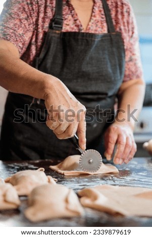 Unrecognizable Latin Elderly Woman using dough cutter knife for Preparing Chilean Beef Empanadas in Her Home Kitchen Royalty-Free Stock Photo #2339879619