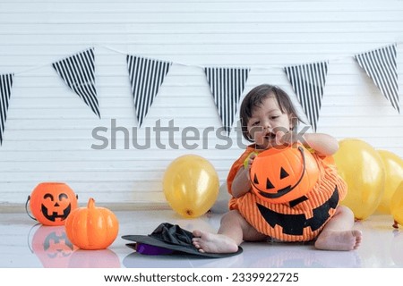 Cute baby girl wearing Halloween pumpkin costume, play trick-or-treating with a pumpkin basket, celebration Halloween party at home 