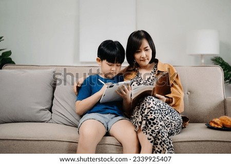 Happy asian mother and son sitting on family couch looking social media on smartphone with children hold laptop phone digital tablet having fun at home,