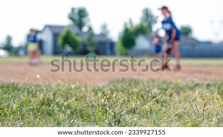 Selective focus on grass with blurred girls softball game in the background