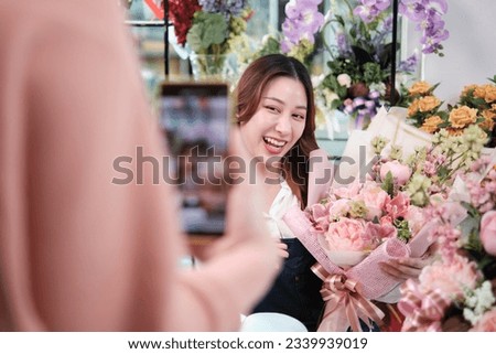 E-commerce business, young Asian female florist worker demonstrates and shows floral arrangements via online live streaming by smartphone application in bright flower shop, beautiful blossoms store. 