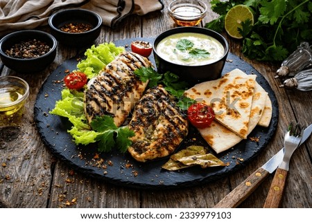 Grilled chicken breast, pita bread and fresh vegetables on wooden table 