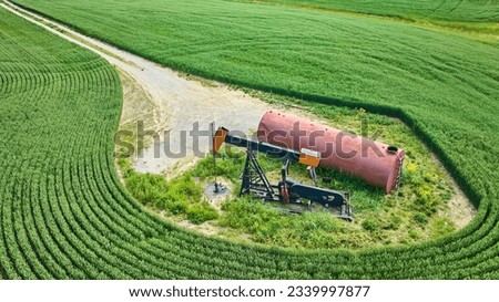 Oil pump jack and tank in field with maintenance road aerial