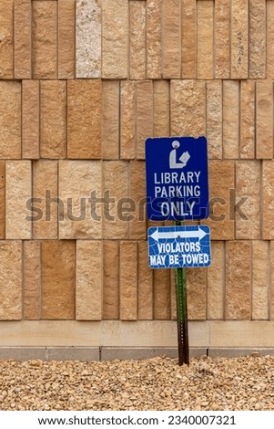 Close up view of a library parking sign in front of an attractive modern limestone wall with unique rough textured vertically aligned natural stone bricks