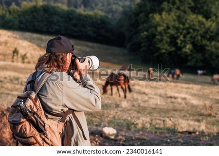 Photographer with camera and telephoto lens taking picture of horse on pasture