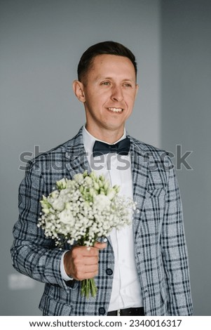 Handsome happy groom with bouquet white flowers roses and gypsophila. Portrait of man. Wedding bouquet in grooms hands. Morning preparation. Man getting dressed and preparing for wedding. Closeup