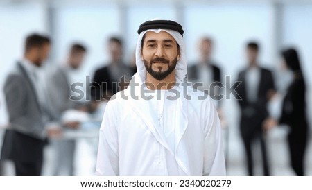 Middle East Arab man in Kandura at office with colleagues coworker workmates at background. Emirati national businessman on dishdasha ideal for Middle Eastern diversity concept. Royalty-Free Stock Photo #2340020279
