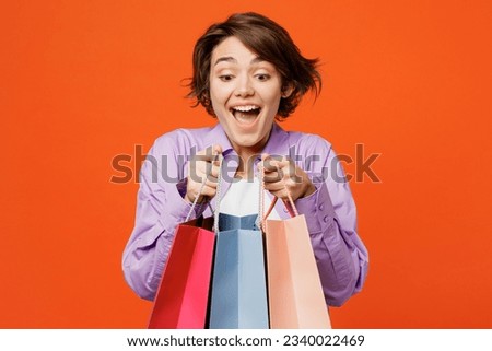 Young surprised woman wears purple shirt casual clothes hold in hand open paper package bags after shopping isolated on plain light orange color background studio. Black Friday sale buy day concept