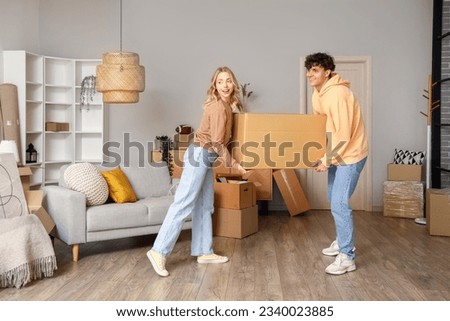 Young couple carrying cardboard box in room on moving day Royalty-Free Stock Photo #2340023885