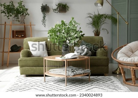 Interior of light living room with green sofa and blooming jasmine flowers on coffee table Royalty-Free Stock Photo #2340024893