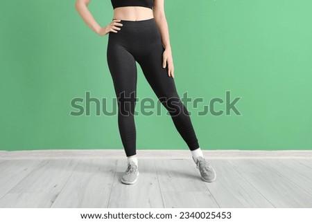 Sporty young woman in leggings near  green wall