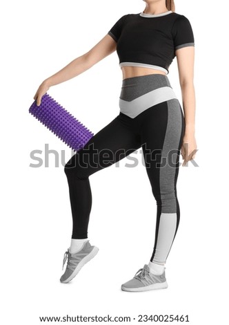 Young woman in sportswear and with foam roller on white background