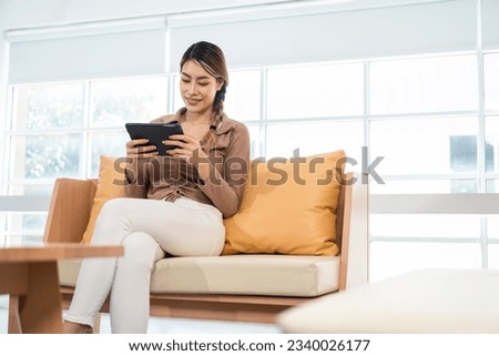 Young asian business woman sitting on sofa in living room at home working with tablet. Young asian beautiful business woman working with tablet sitting sofa at home.