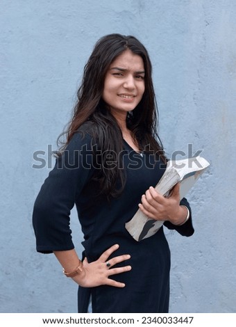 Photo of a beautiful Indian girl student holding a book and looking at the camera. 