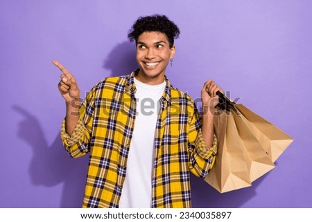 Photo of funky dreamy guy wear plaid yellow shirt holding shoppers looking showing empty space isolated violet color background