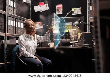 Policewoman looking at holograms in archive space, trying to solve crime with evidence and clues. Private investigator examining holographic photos and augmented reality at table. Royalty-Free Stock Photo #2340043415