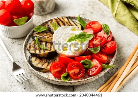 Italian food, snack. Burrata or mozzarella cheese and vegetables, grilled eggplant, tomatoes, basils, grissini.  Royalty-Free Stock Photo #2340044461
