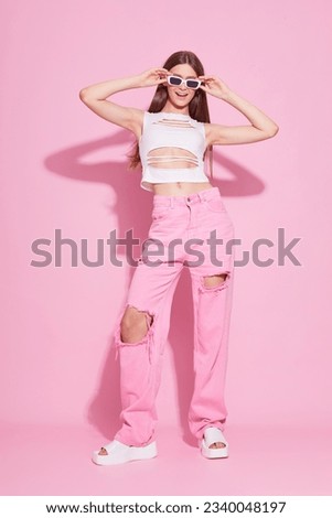 Young fashion woman in pink trendy jeans and white top on pink background. Platform slides sandals, y2k, monochrome, violet bright  makeup. Royalty-Free Stock Photo #2340048197