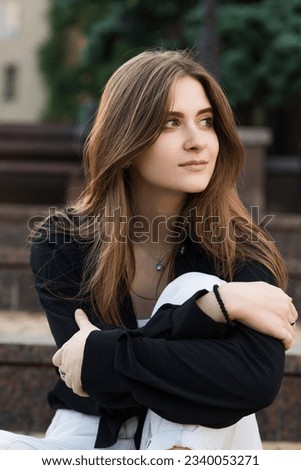 Portrait of a young and attractive happy Caucasian girl sitting on the steps on a summer day in casual clothes. A positive girl enjoys the summer.