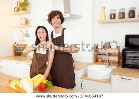Young couple making heart shape with hands Smiling Young happy romantic beautiful woman handsome man in love showing heart symbol look at camera in kitchen Enjoy cooking together Romantic concept Royalty-Free Stock Photo #2340054187