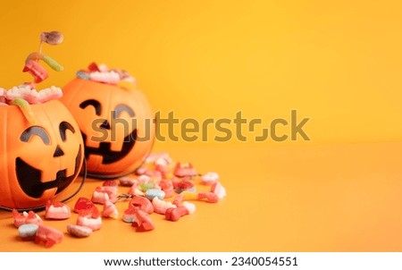 Baskets in the form of pumpkins with sweets on yellow background.