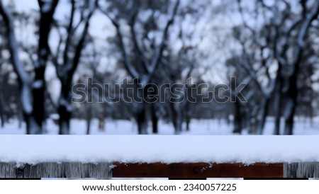 Snow lies atop a wooden fence with a blurred winter forest backdrop, evoking a tranquil, frosty scene. Royalty-Free Stock Photo #2340057225