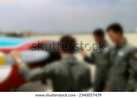 Blurred training photo in airport. Pilot trainer in green uniform teaching about Aircraft flying system and propeller with 2 flyer students in front of multicolor airplane. Royalty-Free Stock Photo #2340057439