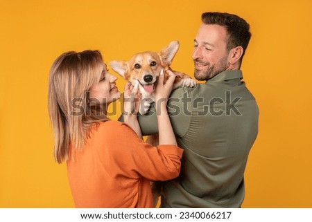Caucasian couple hugging with their corgi dog, happy man and woman in casual clothes with pet on yellow studio background