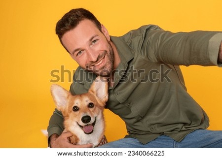 Best friend. Excited european man hugging taking selfie with his corgi dog, posing looking at camera and smiling isolated on yellow studio background, webcam point of view