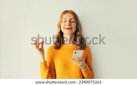Young smiling happy woman with phone having luck keeps calm or meditates with closed her eyes on white background