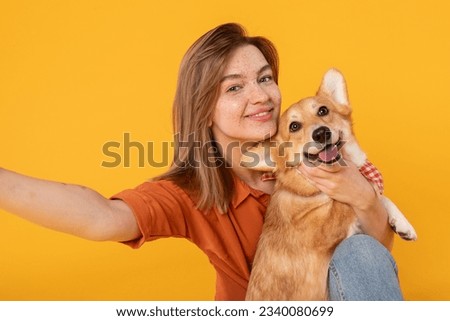 Friendship concept. Happy european woman taking selfie with her cute corgi dog, looking and smiling at camera over yellow studio background wall, closeup