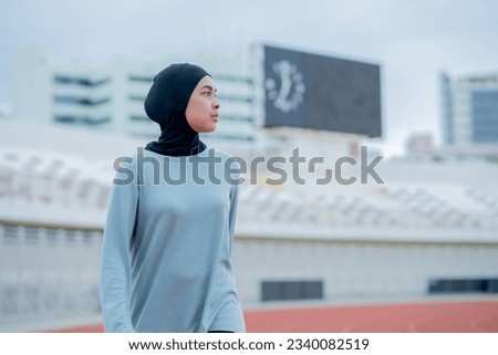 A young asian Muslim woman wearing a black hijab is exercising and running at an outdoor stadium in the morning. Modern Muslim woman concept,  Muslim woman sport concept, Islam